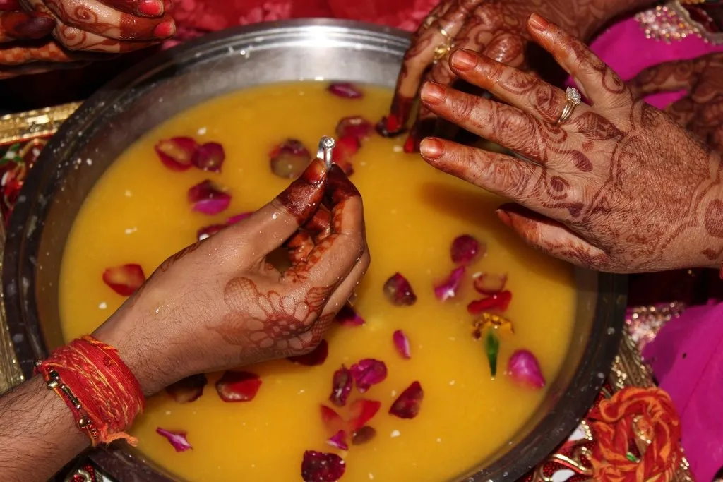 Hands searching for a ring in a bowl of milk and rose petals, a wedding-day game