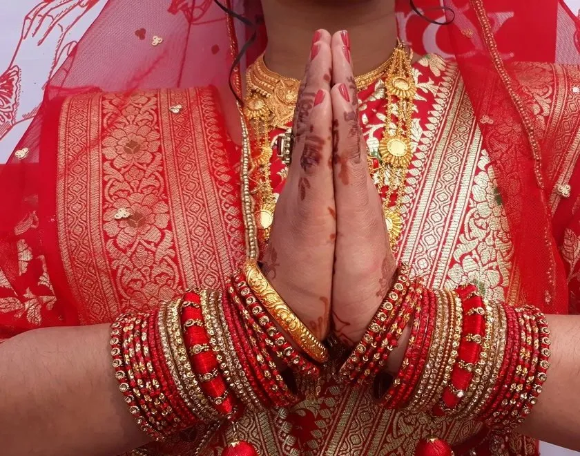 A bride in red and gold with her hands folded in namaste