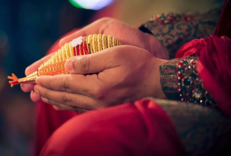 Hands holding a gold-wrapped wedding coconut at an Indian ceremony